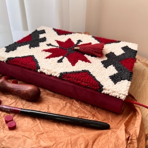 May include: A journal cover with a red, white and black patterned design, featuring a tassel. The cover is made from a thick, textured fabric and has a red velvet spine.