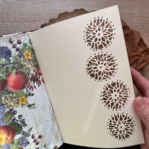 May include: A cream-coloured journal with a floral design on the front cover. The back cover has a decorative pattern of four cut-out circles.