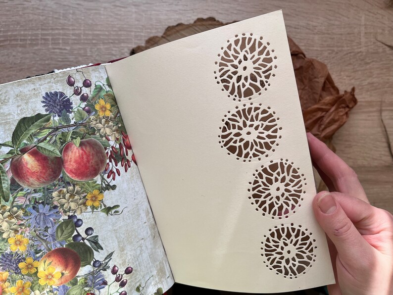 May include: A cream-coloured journal with a floral design on the front cover. The back cover has a decorative pattern of four cut-out circles.