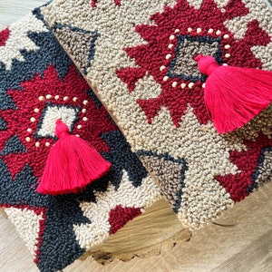 May include: Two handmade needle-punched wool wall hangings with geometric patterns in red, beige, and black. Each piece has a red tassel.