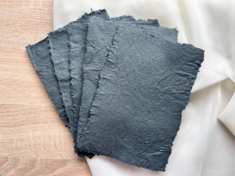 May include: A stack of six sheets of handmade, dark gray paper with deckled edges. The paper has a rough, textured surface.