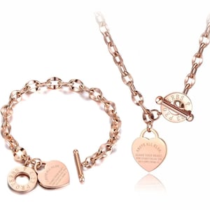May include: A rose gold necklace and bracelet set with a heart charm that reads "Above all else, guard your heart, for everything you do flows from it." The charms are attached to a toggle clasp with the inscription "Pro 4:23 ERBS".