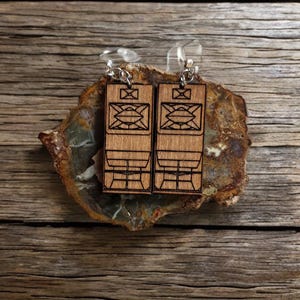 May include: A pair of wooden earrings with a geometric design. The earrings are brown and have a silver hook.