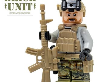 May include: A custom action minifigure of a soldier, holding a tan rifle. The figure wears a tan helmet with night vision goggles, a tan vest, and camouflage pants. The text "BRICK UNIT" and "CUSTOM ACTION MINIFIGURES" are visible.