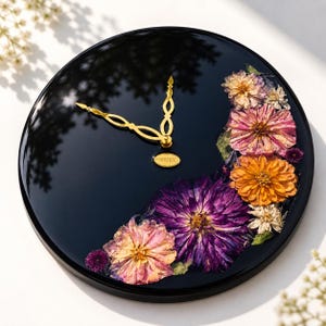Peut inclure: Une horloge murale ronde noire avec des aiguilles dorées et un motif floral. Le cadran de l'horloge présente un groupe de fleurs séchées colorées, notamment des fleurs roses, violettes et oranges. L'horloge porte le mot "VERTESI".