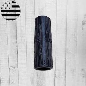 Peut inclure: Un vase cylindrique bleu foncé avec un motif de grain de bois texturé. Le vase est grand et étroit, avec une ouverture circulaire en haut et en bas. Le fond est une surface en bois blanc.