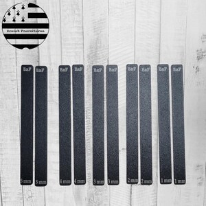 Peut inclure: Plusieurs bandes noires rectangulaires, avec des épaisseurs variant de 1 mm à 5 mm, portant l'inscription "B&F". L'image comprend également un logo circulaire avec du texte et un motif noir et blanc.