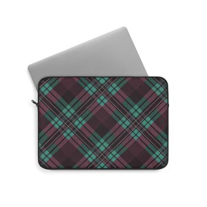 May include: Laptop sleeve with a plaid pattern in shades of burgundy, teal, and white. The sleeve is open, revealing a silver laptop inside. The plaid design features intersecting lines creating a classic tartan look.