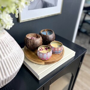 Peut inclure: Quatre bougies de styles et de couleurs diff&eacute;rents, dont une bougie en coque de noix de coco, une bougie &agrave; motifs rose et blanc, une bougie &agrave; motifs bleu et blanc et une bougie jaune avec des fleurs s&eacute;ch&eacute;es sur le dessus. Les bougies sont dispos&eacute;es sur un plateau en bois.