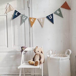 May include: A nursery scene with a white folding chair, a stuffed bunny, and a banner spelling "LUCUS". A white basket with the word "Hello" is on the right. The banner has various colors.