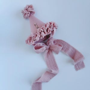 Peut inclure: Chapeau de fête rose poudré avec nœud et ruban assortis. Le chapeau a une garniture à volants et le chiffre "1". Le ruban long est parfait pour une fête de premier anniversaire.