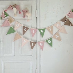 May include: A pink, green, and brown fabric banner with the name "Olivia" spelled out in white letters. The banner is hanging on a white door.