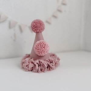May include: A pink party hat with a ruffled trim and two pink pom-poms on top.