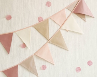 May include: A pink, beige, and white fabric banner with triangle flags strung together. The banner is hanging on a white wall with pink confetti scattered around it.