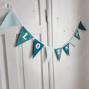 May include: A teal and light blue fabric banner with the name "LORENZO" spelled out in white letters.