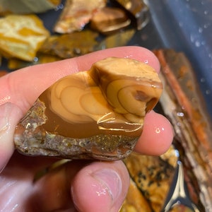 Puede incluir: Primer plano de una piedra de &aacute;gata marr&oacute;n y tostada con un patr&oacute;n de remolino. La piedra est&aacute; mojada y tiene un acabado brillante.