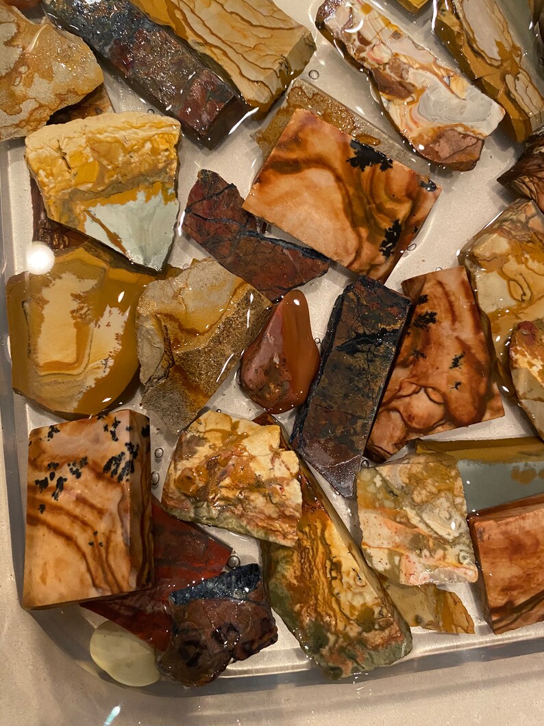 Puede incluir: Una colecci&oacute;n de piedras de &aacute;gata de colores, con patrones y texturas, en diversas formas y tama&ntilde;os. Las piedras est&aacute;n sumergidas en agua, creando un efecto brillante.