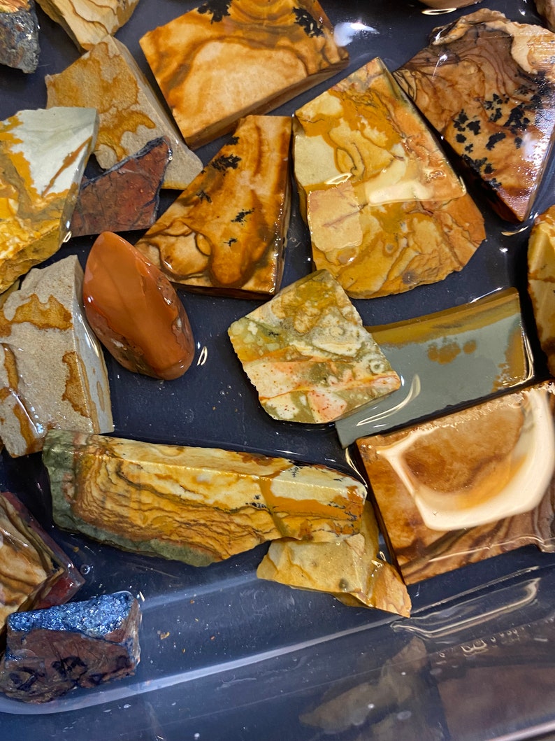 Puede incluir: Una colecci&oacute;n de piedras de &aacute;gata pulidas multicolores con patrones marrones, amarillos, blancos y naranjas. Las piedras est&aacute;n dispuestas sobre una superficie gris oscura.