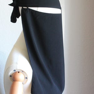 May include: A black niqab, a traditional Islamic veil, is displayed on a mannequin. The veil features a head covering with a tied bow and a long, flowing face covering. The fabric appears to be a matte, opaque material.
