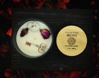 May include: A white soy blend candle in a glass jar with a wooden lid. The candle is decorated with dried rose petals, a silver key, and a clear crystal. The lid is labelled "Petals & Potions, Hecate, Soy Blend Candle, 7 oz | 198 g".