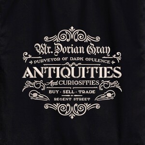 May include: Black tote bag with a white design that reads "Mr. Dorian Gray, Purveyor of Dark Opulence, Antiquities and Curiosities, Buy Sell Trade, Regent Street."