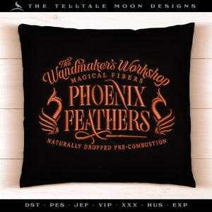 Puede incluir: Una almohada negra con un diseño bordado en naranja que dice "The Wandmaker's Workshop Phoenix Feathers Magical Fibers Naturally Dropped Pre-Combustion".
