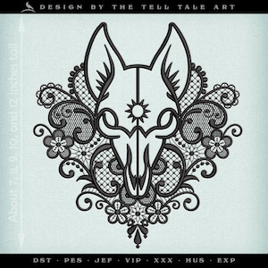 Op de afbeelding: Zwart borduurontwerp met een gestileerde dierenkop met grote oren, een zon-achtig embleem en bloemenkant details. Het ontwerp is ongeveer 18, 20, 23 en 30 cm hoog. De tekst "DESIGN BY THE TELL TALE ART" staat bovenaan.