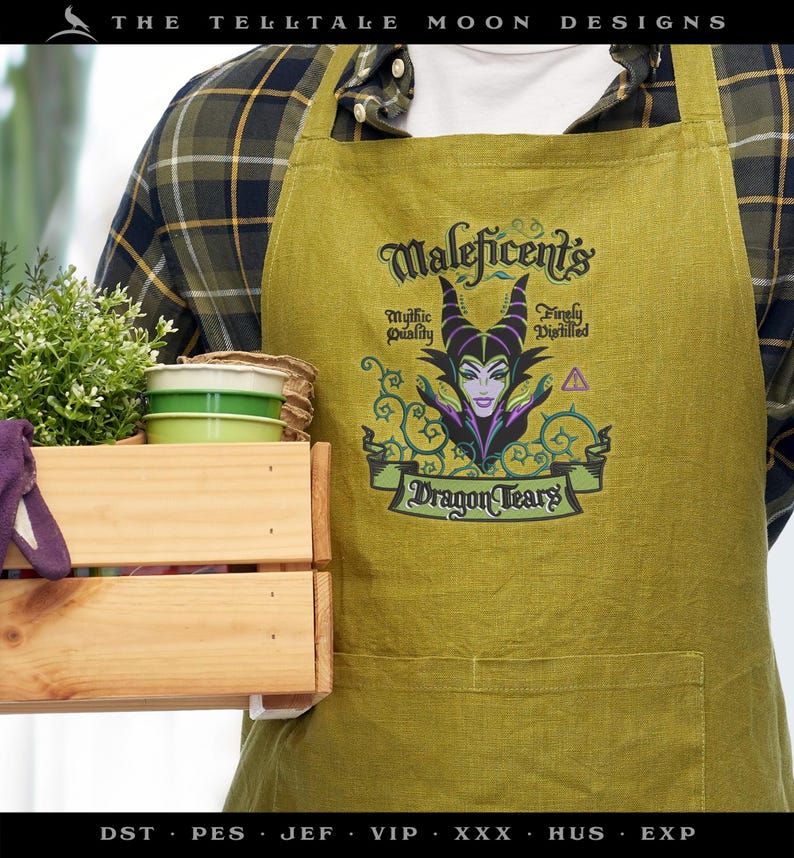 May include: A green apron featuring the text "Maleficent's Dragon Tears" with an illustration of Maleficent. The apron has a pocket and is worn over a plaid shirt. A wooden crate with plants and small green and white containers is in the foreground.