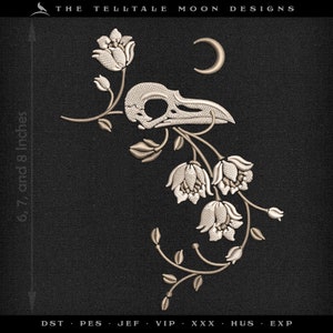 May include: A white embroidered design of a bird skull with a crescent moon above it, surrounded by white flowers and vines on a black background. The text "THE TELLTALE MOON DESIGNS" is at the top of the image.
