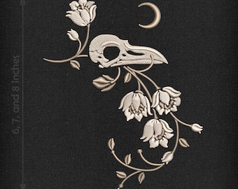 May include: A white embroidered design of a bird skull with a crescent moon above it, surrounded by white flowers and vines on a black background. The text "THE TELLTALE MOON DESIGNS" is at the top of the image.