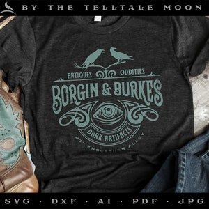 May include: Dark gray t-shirt featuring the text "BORGIN & BURKES" in a vintage style, with the words "ANTIQUES ODDITIES" above and "DARK ARTIFACTS" below. The design includes an eye symbol and two birds. The shirt is displayed with cowboy boots and jeans.