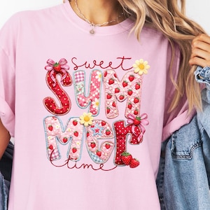 May include: Pink t-shirt with the words "Sweet Summer Time" in a colorful, patchwork design. The letters are decorated with strawberries, flowers, and bows. The shirt is a light pink color.