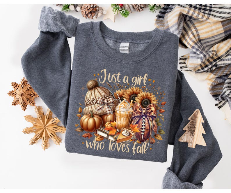 May include: Dark gray sweatshirt with a fall-themed graphic. The graphic includes a knitted hat, pumpkins, sunflowers, a football, and a beverage. Text on the sweatshirt reads "Just a girl who loves fall."