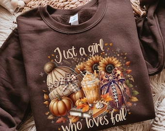 Könnte beinhalten: Braunes Sweatshirt mit einem herbstlichen Motiv. Das Design umfasst Sonnenblumen, Kürbisse, eine Strickmütze, einen Football, einen Pumpkin Spice Latte und den Text "Just a girl who loves fall."