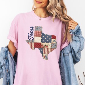 May include: A light pink t-shirt featuring a patchwork design of the state of Texas. The Texas outline is filled with various patterns, including stars, stripes, and floral prints. The word "Texas" is written in a cursive font.