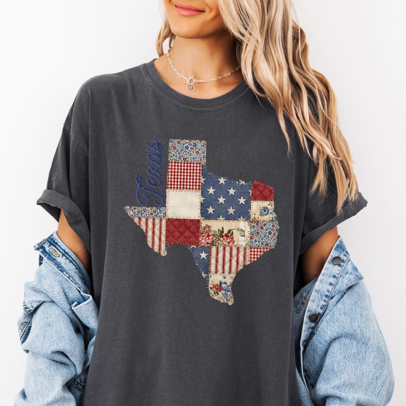 May include: Dark gray t-shirt featuring a patchwork design of the state of Texas. The Texas outline is filled with red, white, and blue patterns, including stars, stripes, and floral prints. The word "Texas" is written vertically in blue.