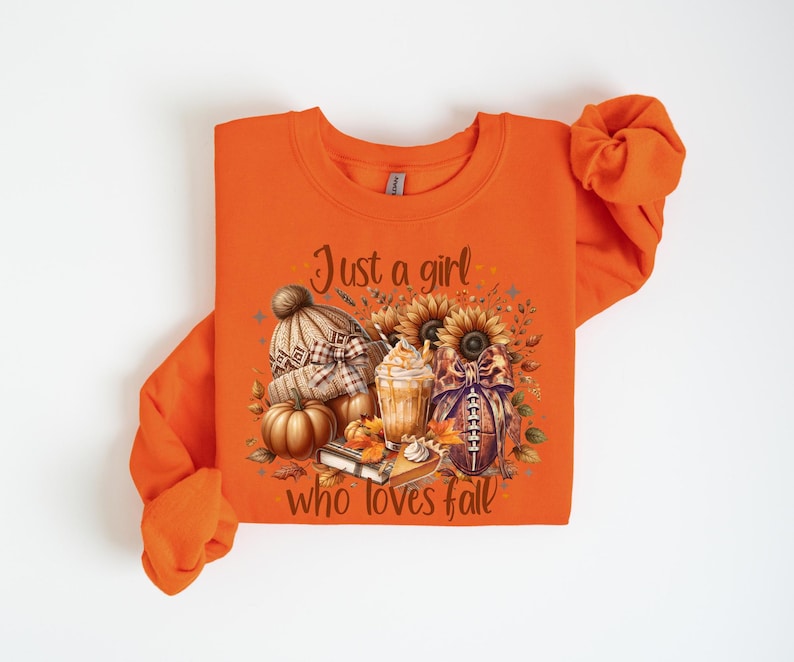 May include: Orange sweatshirt with a fall-themed graphic. The graphic includes a knit hat, pumpkins, sunflowers, a football, and a coffee drink. Text on the shirt reads "Just a girl who loves fall."