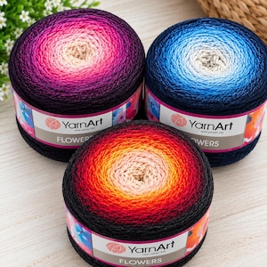 May include: Three round cakes of YarnArt Flowers yarn, each featuring a gradient color transition from a light center to a dark outer edge. One cake transitions from cream to magenta and dark purple, one from cream to blue, and one from cream to orange, red, and black.