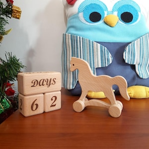 May include: Wooden block calendar with the word "Days" on the top block and the numbers "2", "6", and "2" on the bottom blocks. A wooden toy rocking horse is in the foreground.