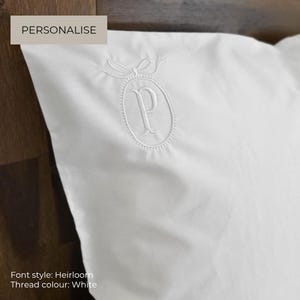 May include: A crisp white pillowcase featuring an elegant white embroidered monogram of the letter P. The letter is centred within an oval frame topped with a decorative bow. The text PERSONALISE is visible in the upper left corner.