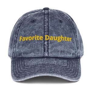Op de afbeelding: Een denimblauwe baseballcap met de geborduurde tekst "Favorite Daughter" in geel. De cap heeft een gebogen klep en een verstelbare band aan de achterkant. Een klassieke stijl, geschikt voor vrijetijdskleding.