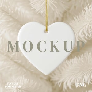 Op de afbeelding: Een witte hartvormige ornament met het woord "MOCKUP" in grijze tekst. De ornament hangt aan een gouden draad tegen een vage witte achtergrond. De woorden "INSTANT DOWNLOAD" en "PNG" zijn ook zichtbaar.