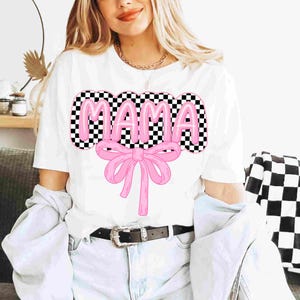 May include: White t-shirt with a pink "MAMA" graphic with a checkered background and a pink bow.