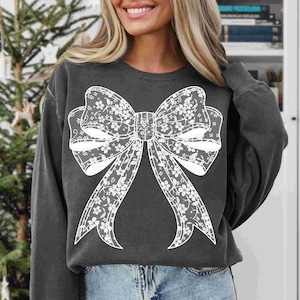 May include: A dark gray sweatshirt with a white lace bow design. The bow is large and centered on the front of the sweatshirt.
