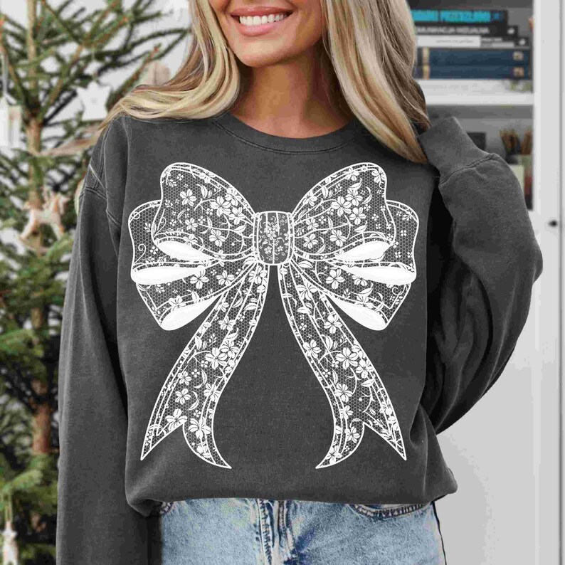 May include: A dark gray sweatshirt with a white lace bow design. The bow is large and centered on the front of the sweatshirt.