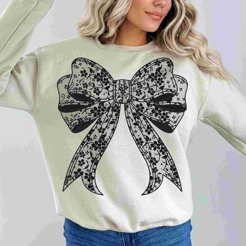 May include: A light beige sweatshirt with a large black lace bow design on the front.