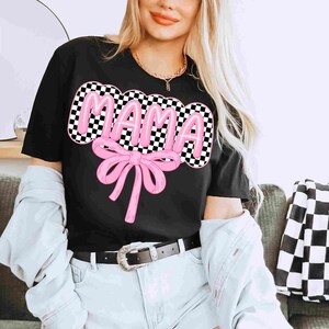 May include: Black t-shirt with a pink "MAMA" graphic in a checkered pattern with a pink bow.