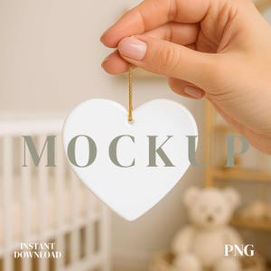May include: A white heart-shaped ornament with the word "MOCKUP" printed on it, suspended by a gold string. The ornament is held by a hand with painted nails. The words "INSTANT DOWNLOAD" and "PNG" are also visible.