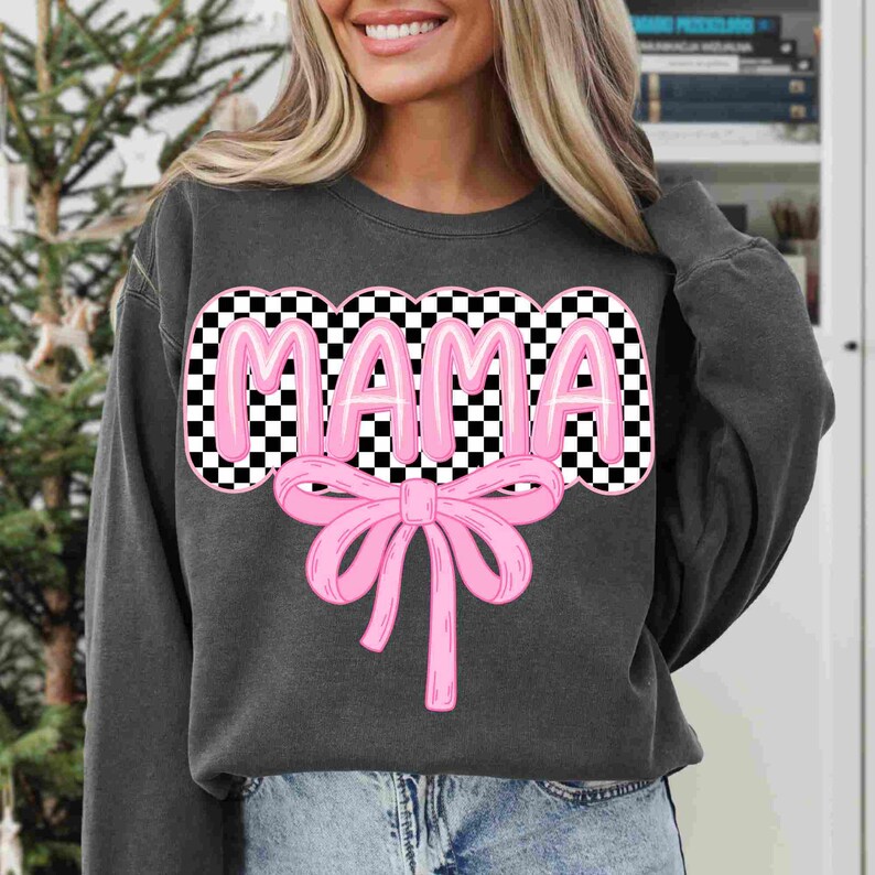 May include: A dark gray sweatshirt with a checkered design and the word "MAMA" in pink letters. A pink bow is below the word.
