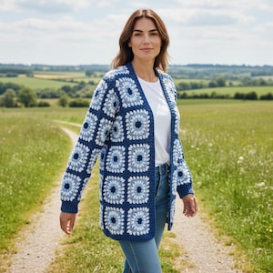 May include: A long-sleeved cardigan made of crocheted granny squares in shades of navy blue, light blue, and white. The open-front garment features a repeating floral-inspired pattern, ribbed cuffs, and a straight hem, worn over a plain white t-shirt.